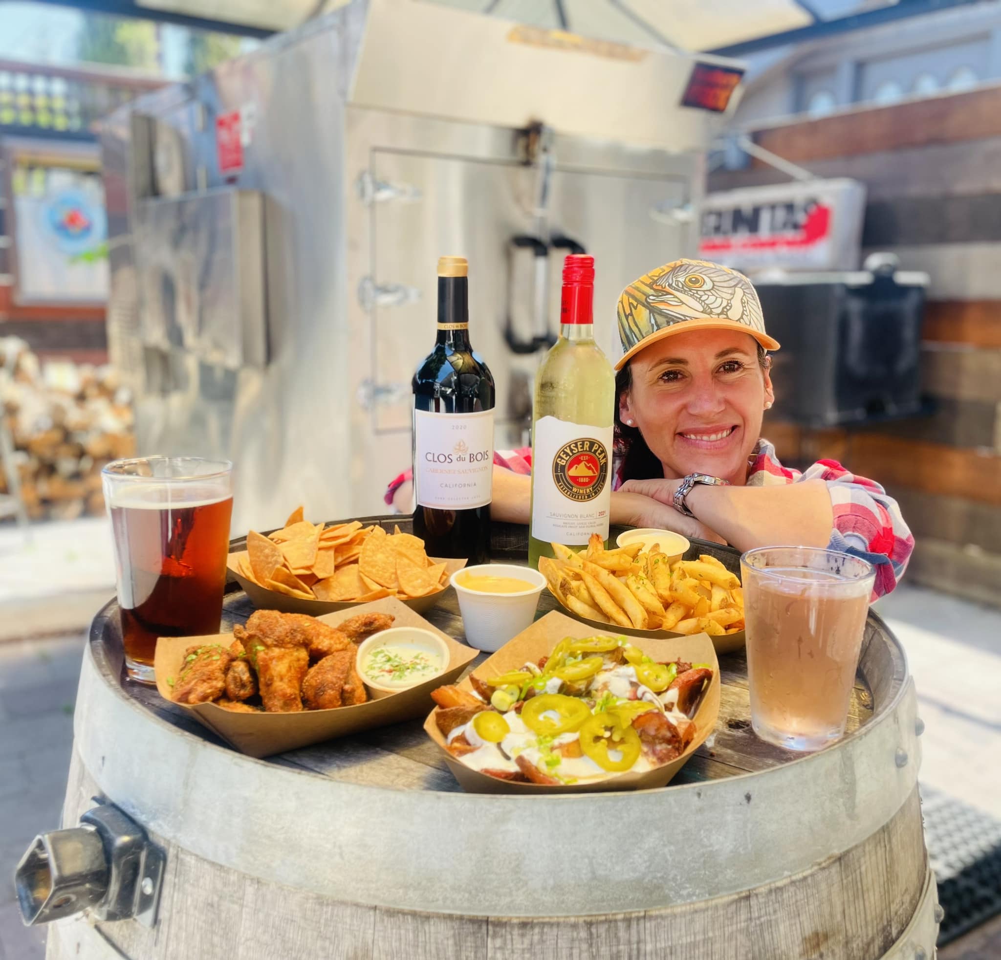 Blazers Smokehouse & Beer Garden in Downtown Novato, California. Owner smiling with an array of their happy hour food offerings, plus beer and wine.