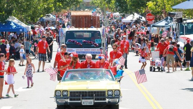 Downtown Novato 4th of July parade. People in a yellow car wearing red and waving American flags.