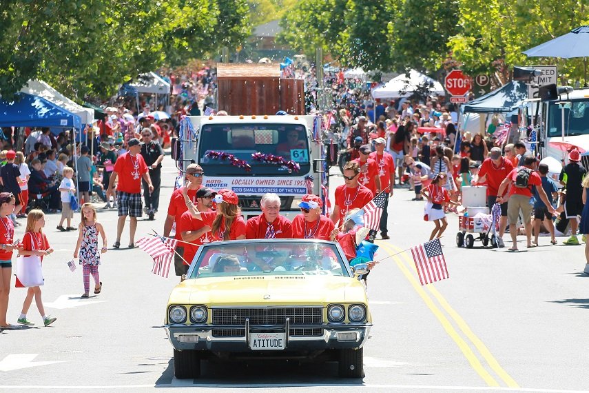 Downtown Novato 4th of July parade. People in a yellow car wearing red and waving American flags.